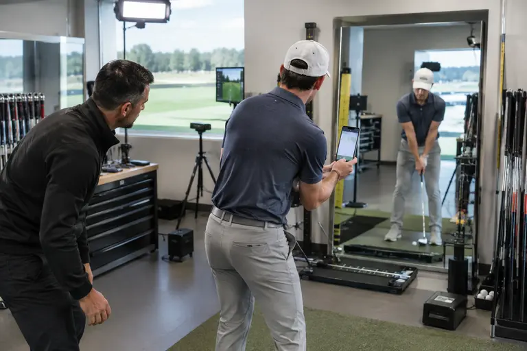 Fitter and golfer reviewing shot notes beside a launch monitor