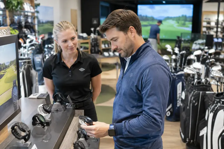 Golfer comparing a smartwatch and clubs on a shop counter