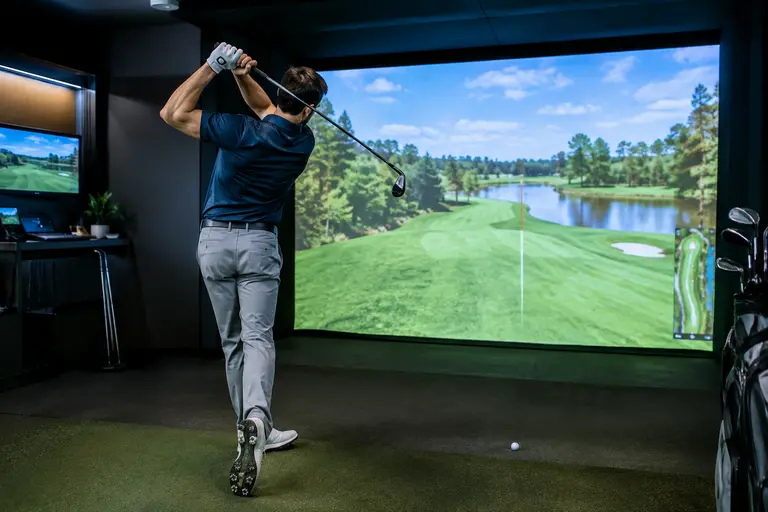 Indoor golf practice area with a putting surface and launch monitor bay nearby